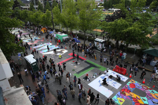 High angle shot of people gathered at CHAZ CHOP street protest in Seattle with Black Lives Matter mural painted on the ground.